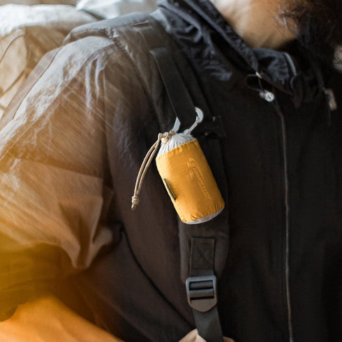 Person wearing a dark coat with a yellow sleeping bag attached to their backpack